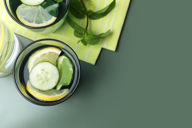 Refreshing water with cucumber, lemon and mint on green table, flat lay. Space for text