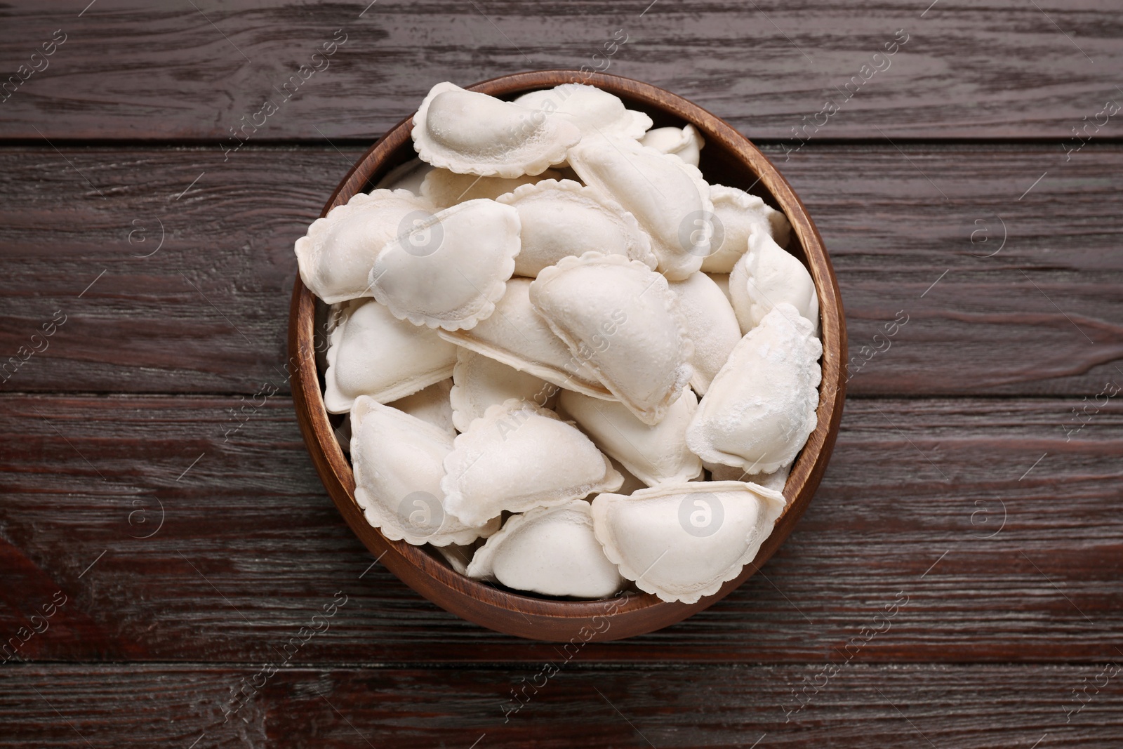 Photo of Raw dumplings (varenyky) on brown wooden table, top view