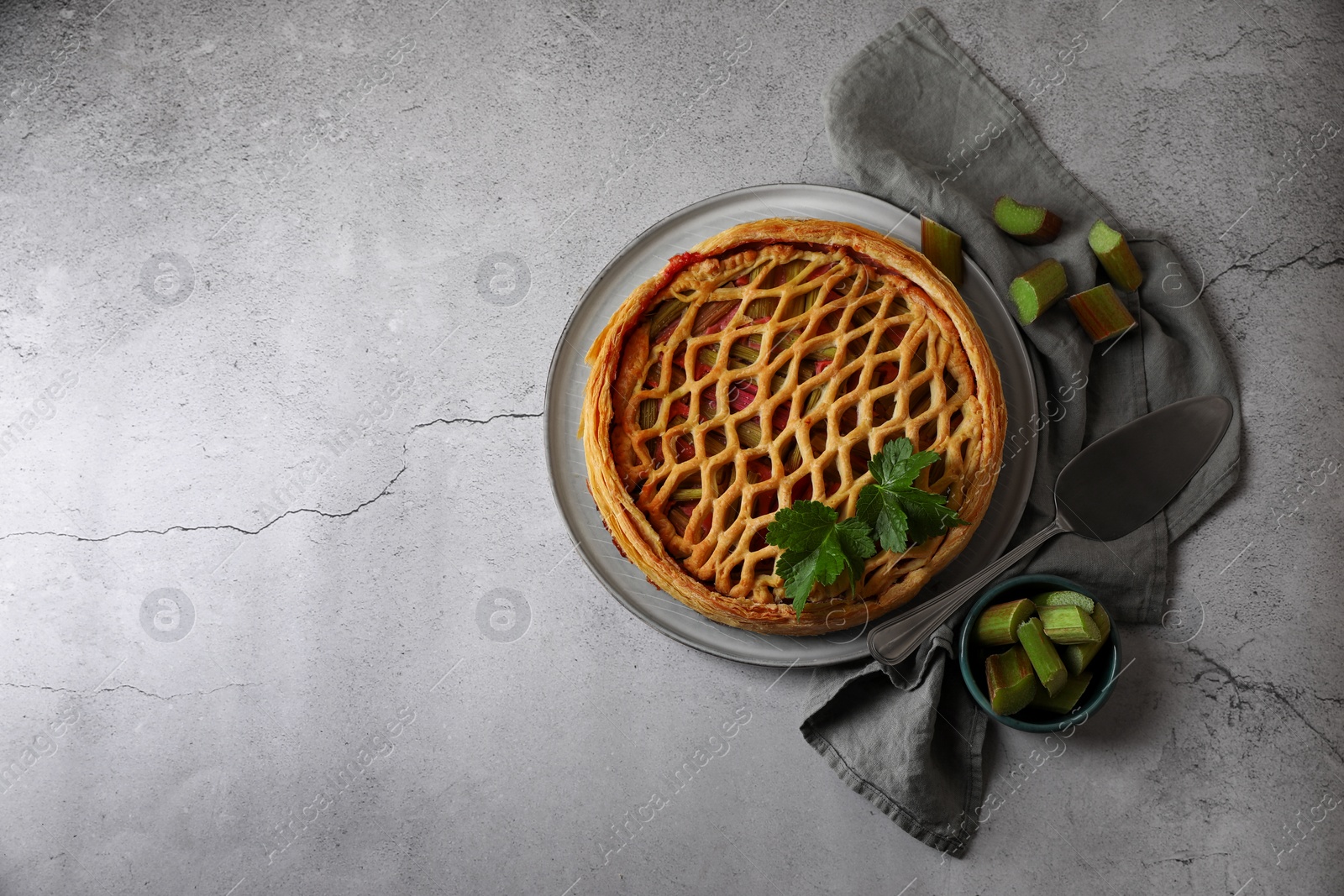 Photo of Freshly baked rhubarb pie, cut stalks and cake server on light grey table, flat lay. Space for text