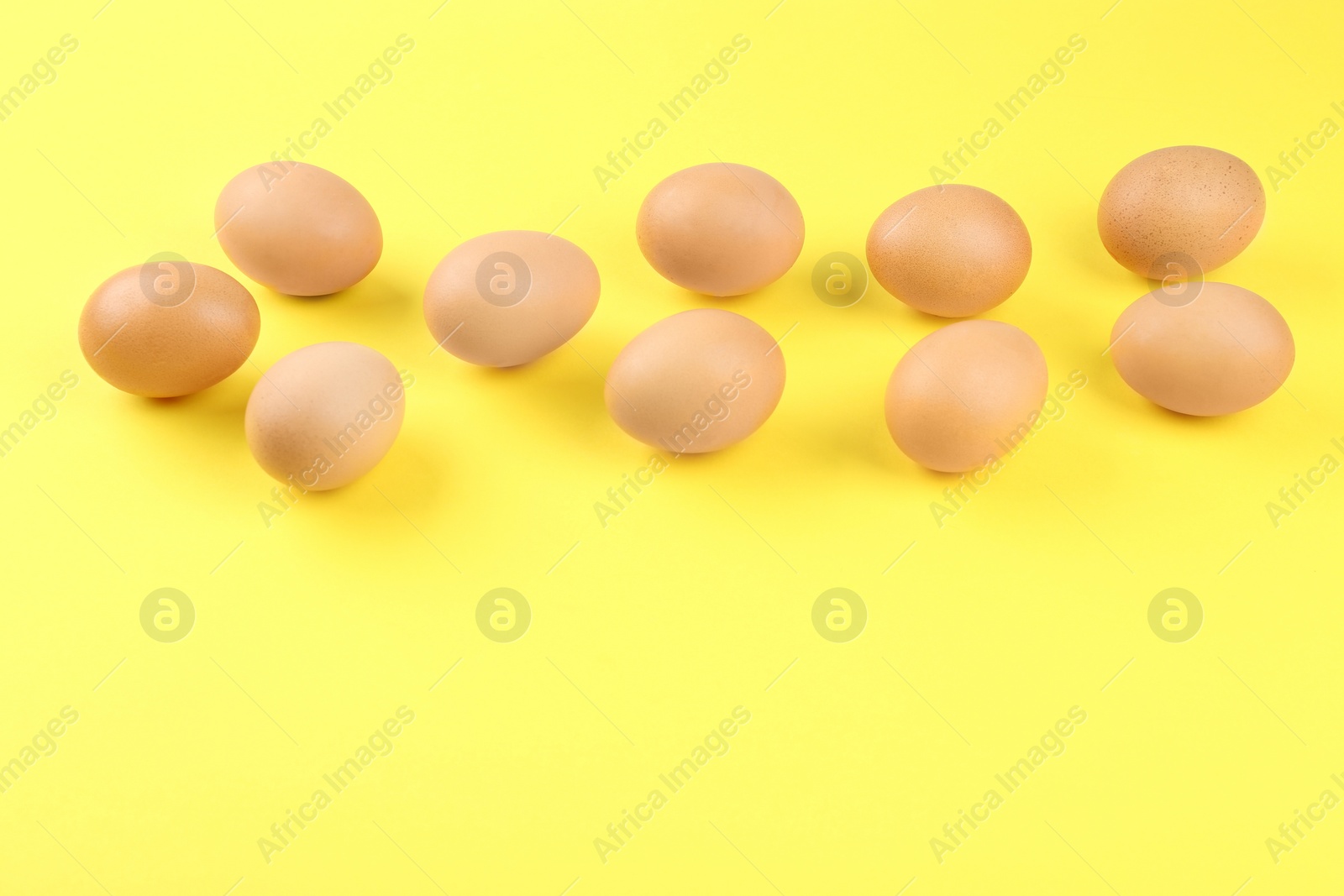 Photo of Raw chicken eggs on yellow background, above view. Space for text