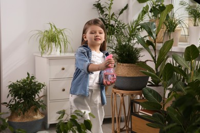 Photo of Cute little girl spraying beautiful green plant at home. House decor