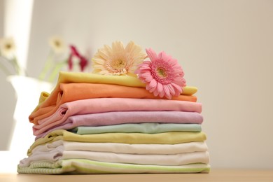 Photo of Stack of clean clothes and flowers on table