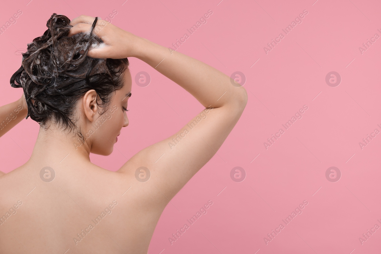 Photo of Woman washing hair on pink background, back view. Space for text