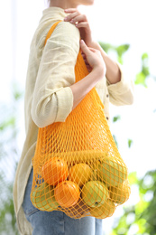 Photo of Woman with net bag full of fruits outdoors, closeup