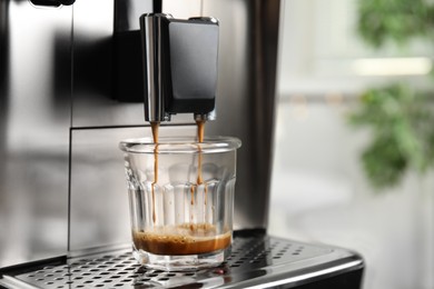 Espresso machine pouring coffee into glass against blurred background, closeup. Space for text