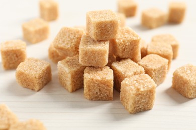 Photo of Heap of brown sugar cubes on white wooden table, closeup