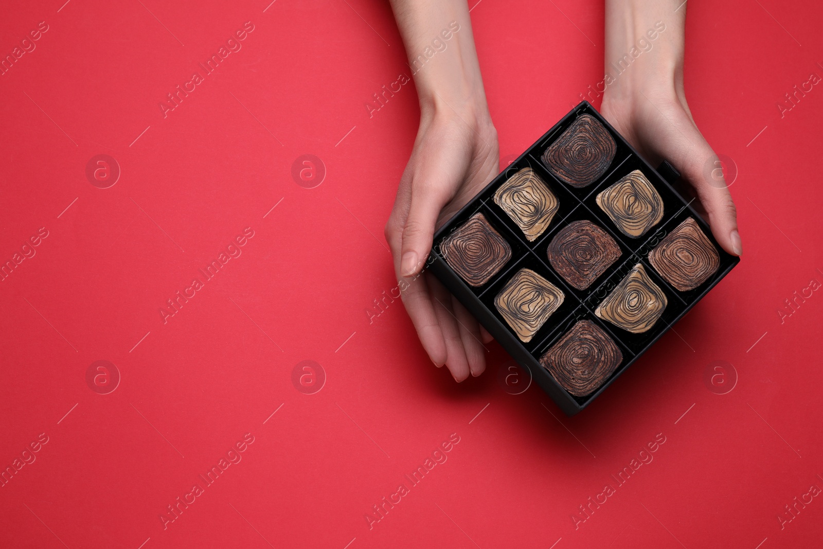 Photo of Woman with box of delicious chocolate candies on red background, top view. Space for text