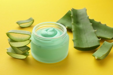 Photo of Jar with cream and cut aloe leaves on yellow background, closeup