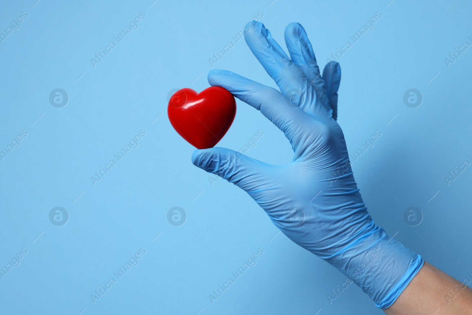 Photo of Doctor wearing medical glove holding decorative heart on light blue background, closeup