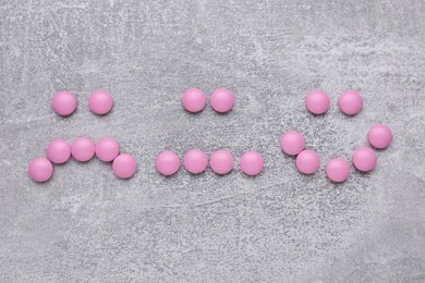Photo of Different emoticons made of pink antidepressants on light grey textured background, flat lay