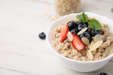 Photo of Tasty oatmeal with strawberries, blueberries and almond petals in bowl on white wooden table, closeup. Space for text