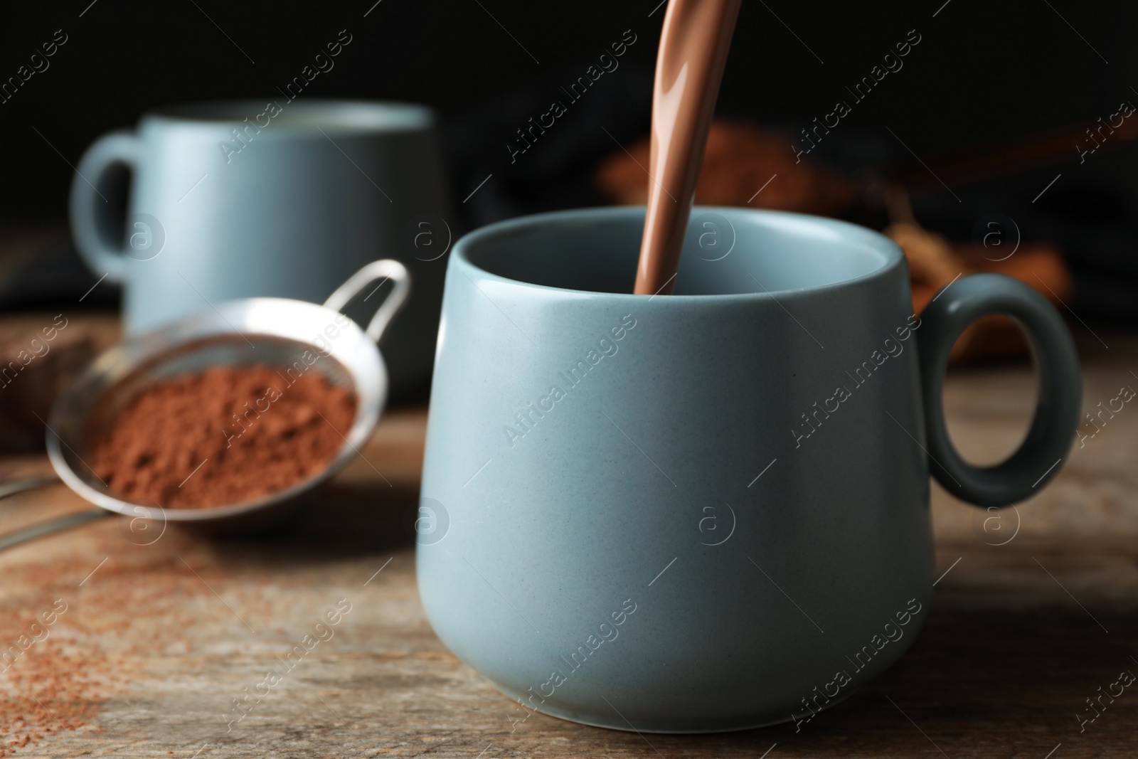 Photo of Pouring hot cocoa drink into cup on wooden table