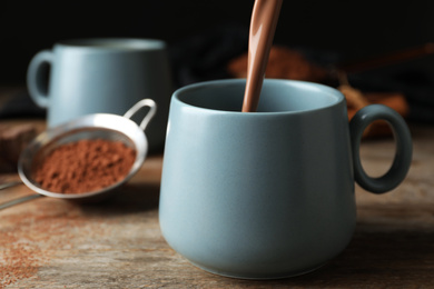 Photo of Pouring hot cocoa drink into cup on wooden table