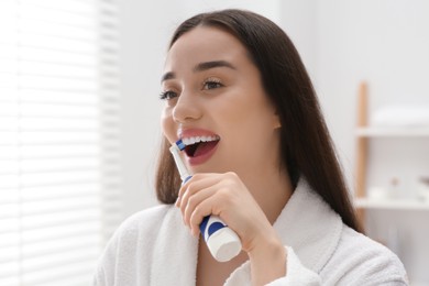 Photo of Young woman brushing her teeth with electric toothbrush in bathroom