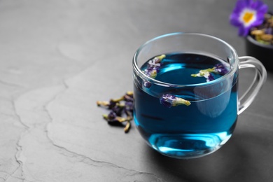 Photo of Glass cup of organic blue Anchan on black table, space for text. Herbal tea