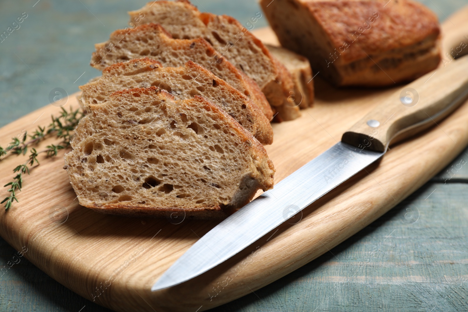 Photo of Cut buckwheat baguette with knife and thyme on light blue wooden table, closeup