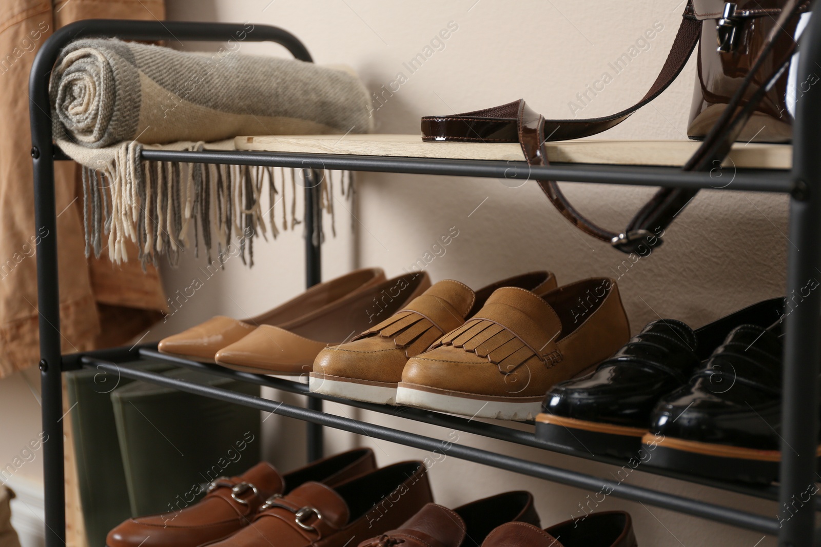 Photo of Rack with different shoes near beige wall, closeup