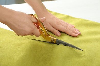 Seamstress cutting light green fabric with scissors at workplace, closeup
