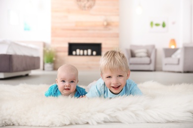 Photo of Cute boy with his little sister lying on fur rug at home