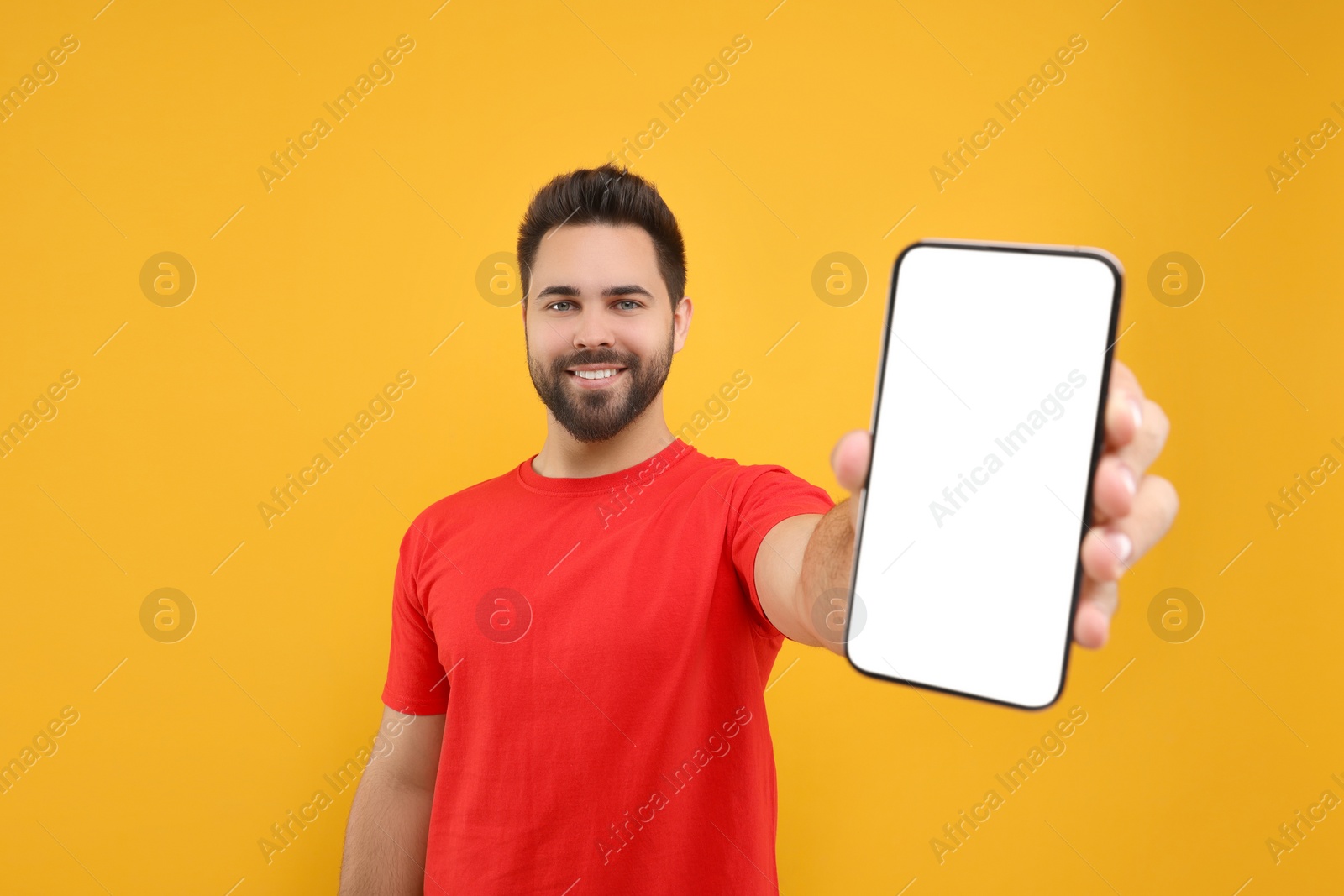 Photo of Young man showing smartphone in hand on yellow background