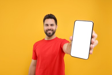 Photo of Young man showing smartphone in hand on yellow background