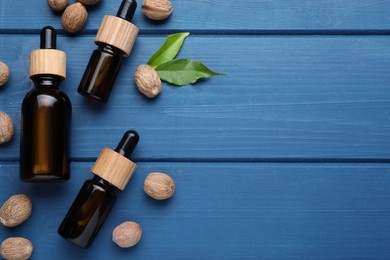 Photo of Bottles of nutmeg oil and nuts on blue wooden table, flat lay. Space for text