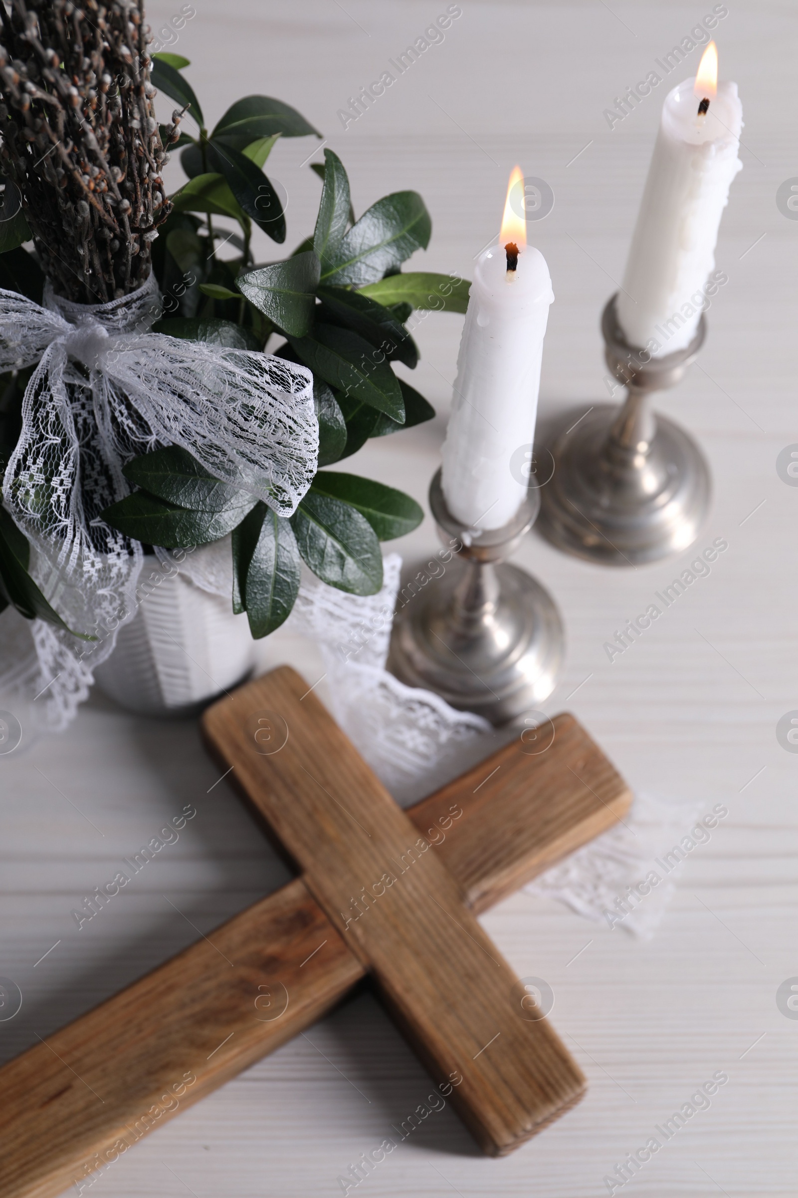 Photo of Burning candles, bouquet with willow branches and cross on white wooden table, above view