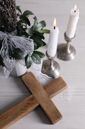 Burning candles, bouquet with willow branches and cross on white wooden table, above view