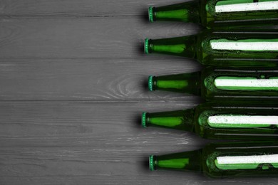 Glass bottles of beer on grey wooden background, flat lay. Space for text