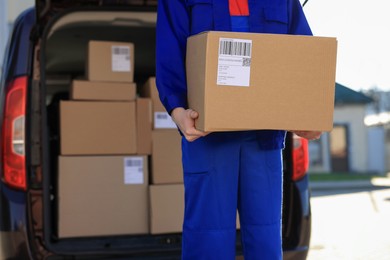 Courier with parcel near delivery van outdoors, closeup. Space for text