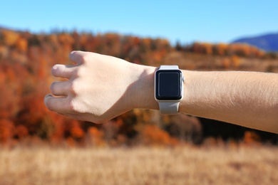 Woman checking smart watch with blank screen in wilderness, closeup