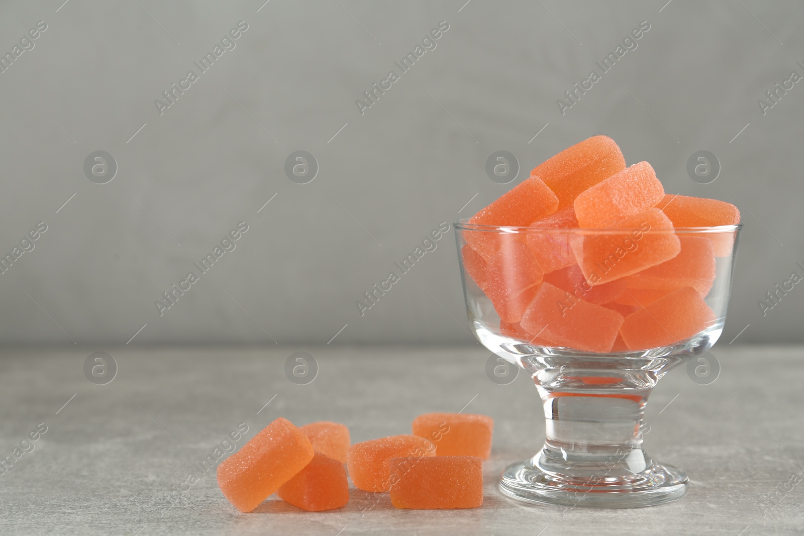 Photo of Tasty orange jelly candies in glass dessert bowl on grey background. Space for text
