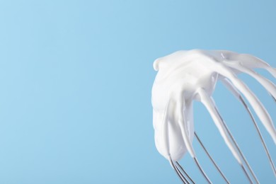 Photo of Whisk with whipped cream on light blue background, closeup. Space for text