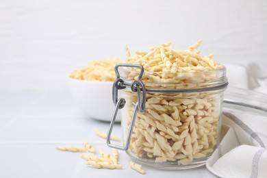 Photo of Uncooked trofie pasta on white tiled table, closeup. Space for text