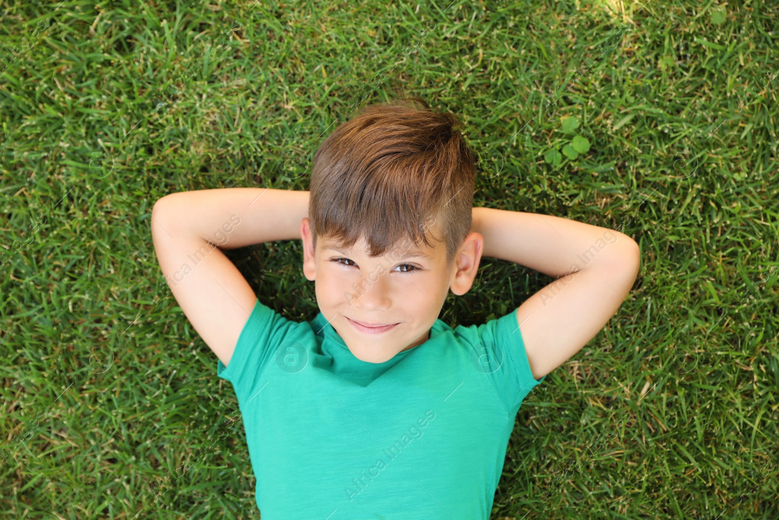 Photo of Cute little boy on green grass in park, top view. Happy child