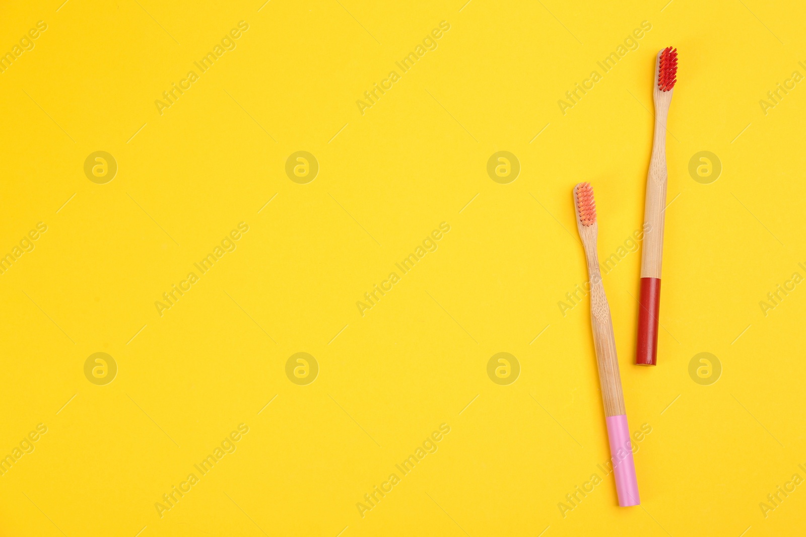 Photo of Toothbrushes made of bamboo on yellow background, flat lay. Space for text