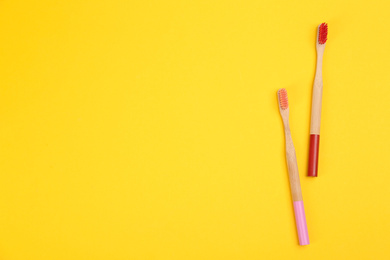 Photo of Toothbrushes made of bamboo on yellow background, flat lay. Space for text