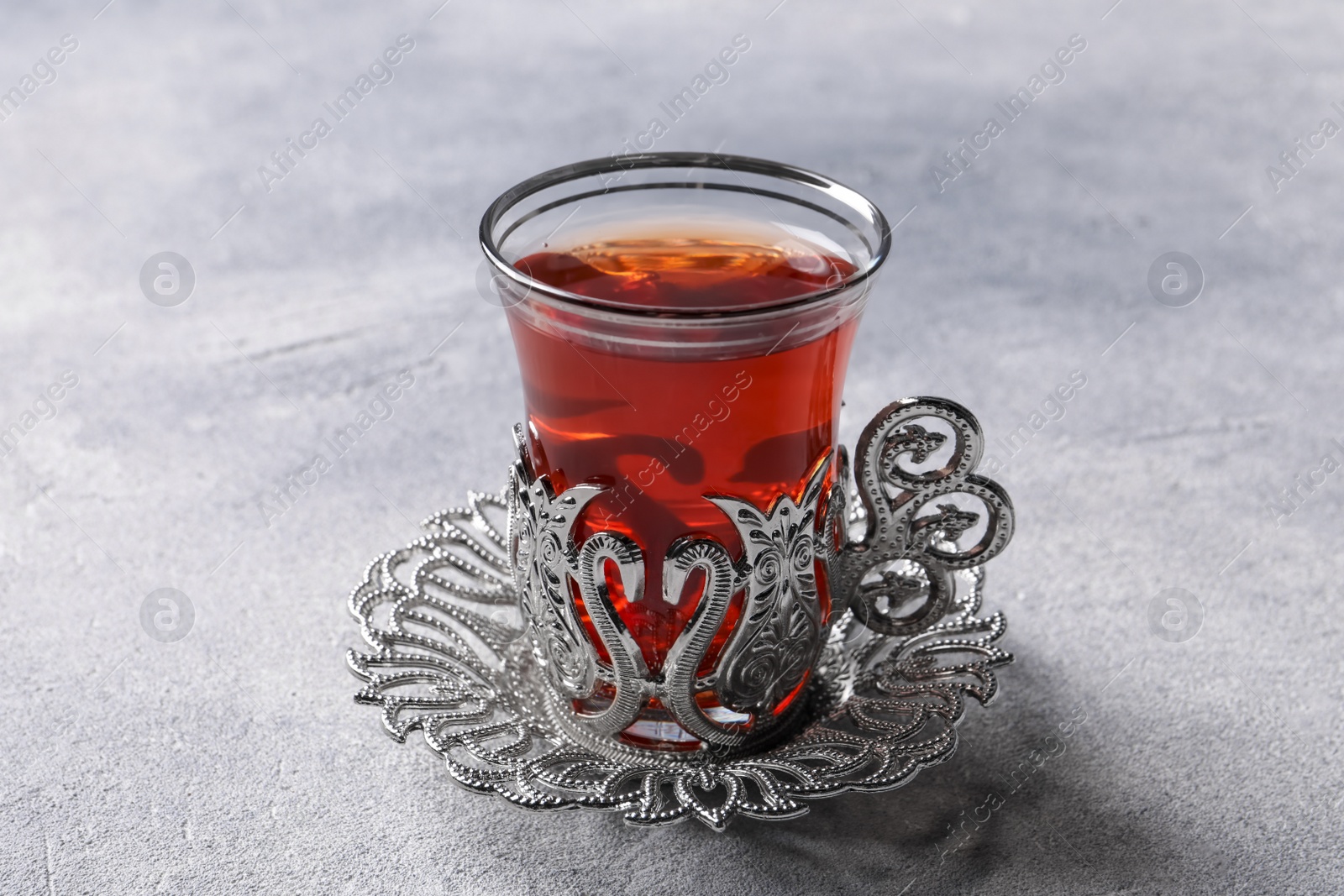 Photo of Glass of traditional Turkish tea in vintage holder on light grey table, closeup