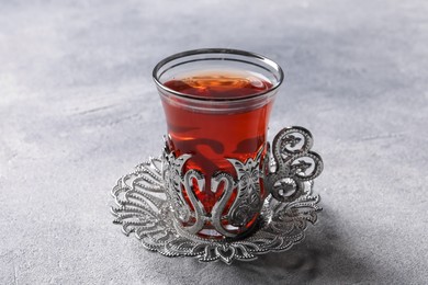 Glass of traditional Turkish tea in vintage holder on light grey table, closeup