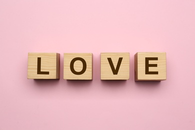Photo of Wooden cubes with word Love on pink background, flat lay