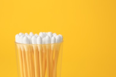 Photo of Container with new cotton buds on yellow background, closeup. Space for text