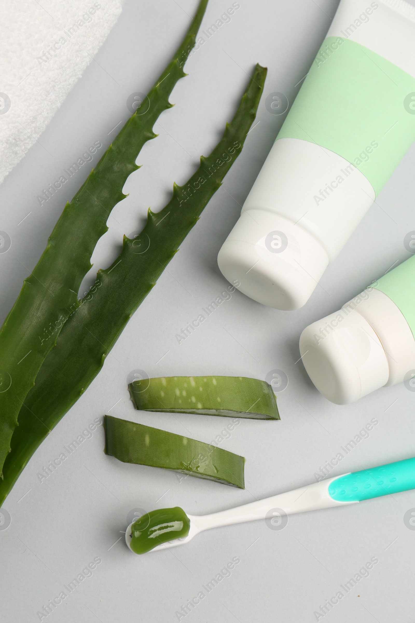 Photo of Tubes of toothpaste, toothbrush and fresh aloe on light grey background, flat lay