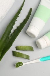 Tubes of toothpaste, toothbrush and fresh aloe on light grey background, flat lay