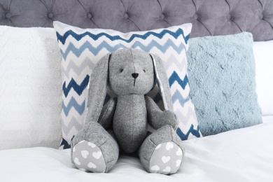 Photo of Cute toy rabbit sitting on bed indoors