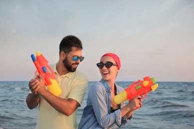 Photo of Happy couple with water guns near sea at sunset