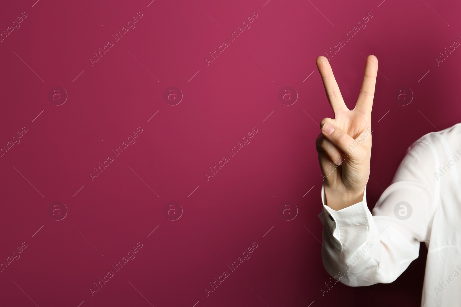 Photo of Young woman showing victory gesture on color background. Space for text