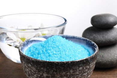 Light blue sea salt in bowl, spa stones and flowers on table against white background, closeup