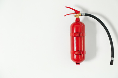 Photo of Fire extinguisher hanging on white wall, space for text