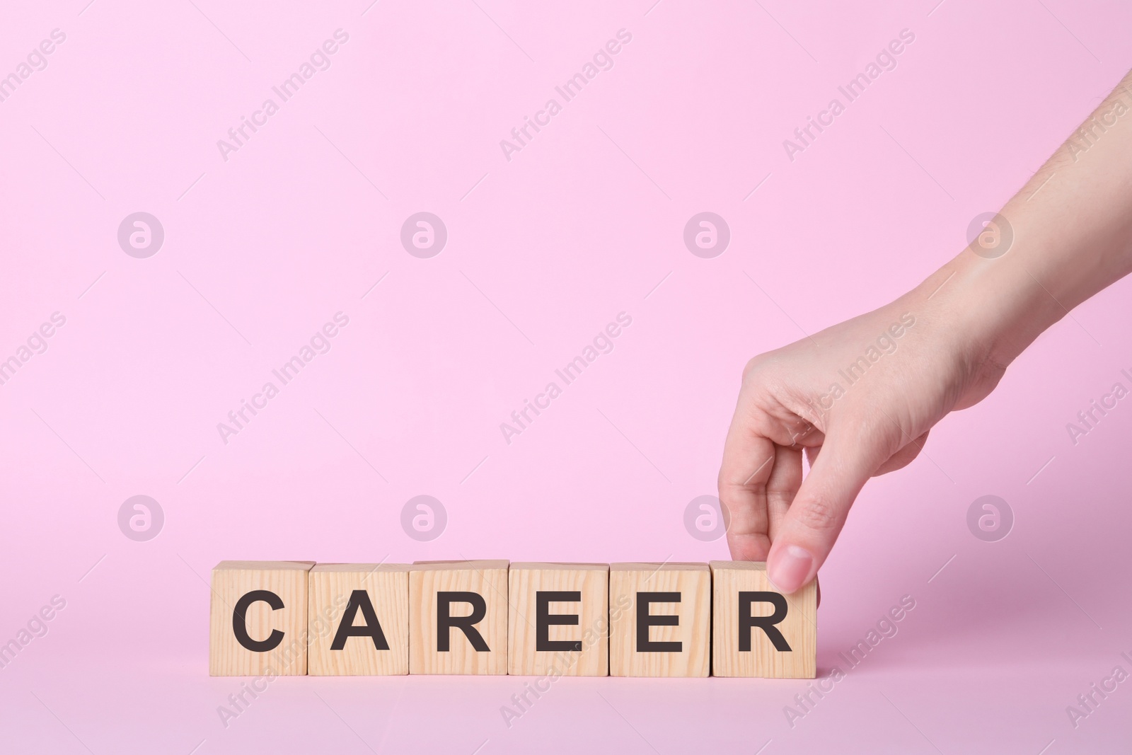 Photo of Woman making word CAREER with wooden cubes on pink background, closeup. Space for text