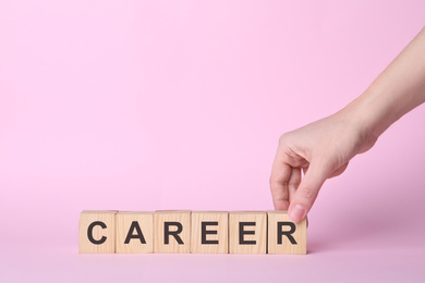 Woman making word CAREER with wooden cubes on pink background, closeup. Space for text